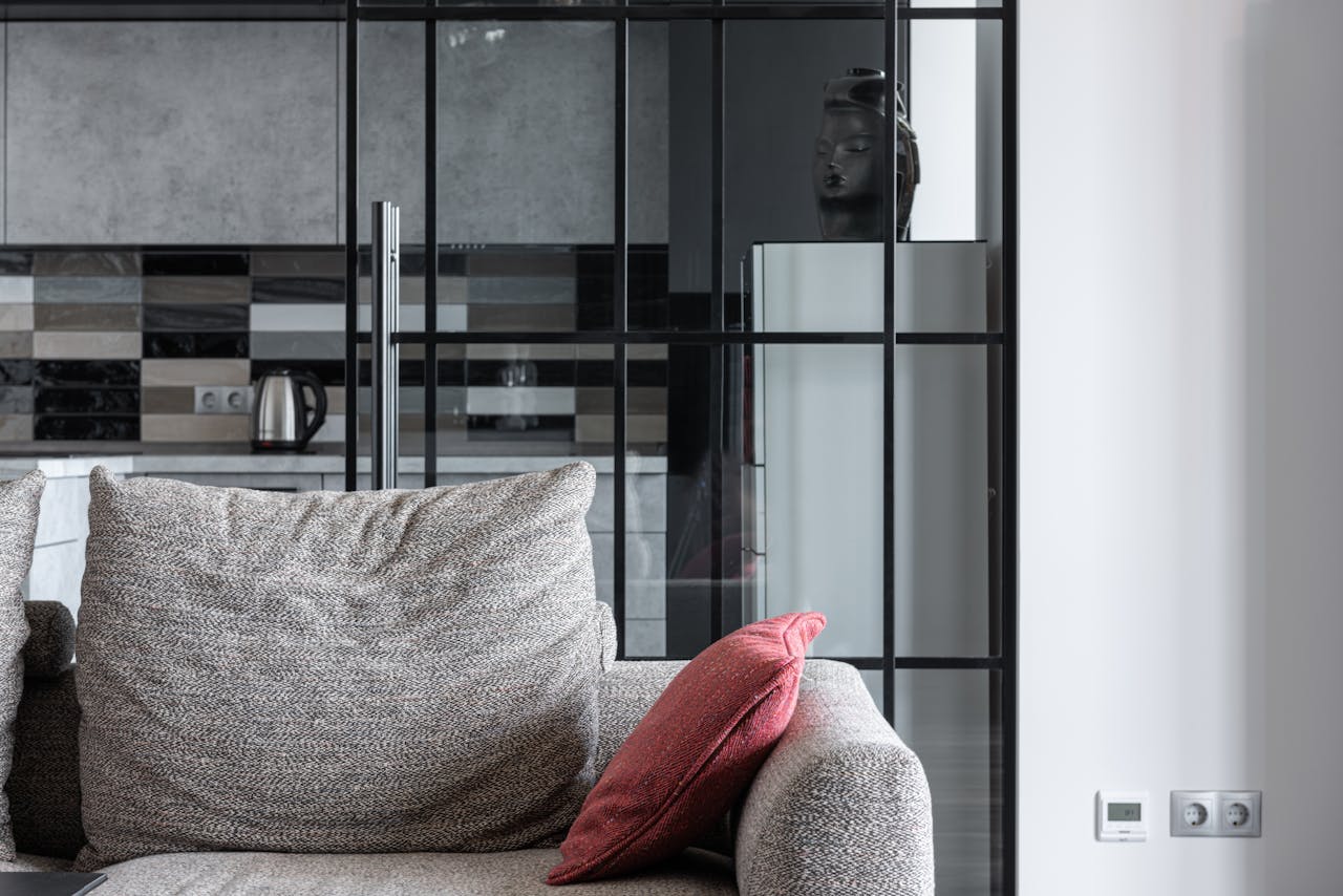 Cozy living room featuring a textured sofa with a red pillow and a modern kitchen backdrop.